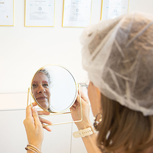 Frau sieht sich in den Spiegel und bewundert Microblading Ergebnis
