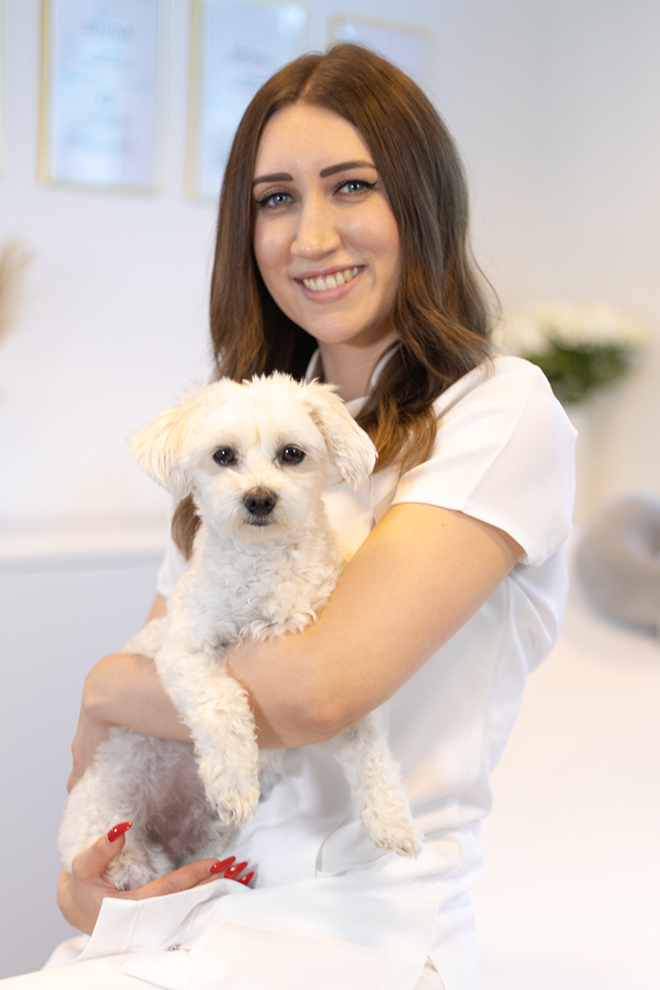 Patricia Portraitfoto mit kleinem Hund im Arm, grinsend.