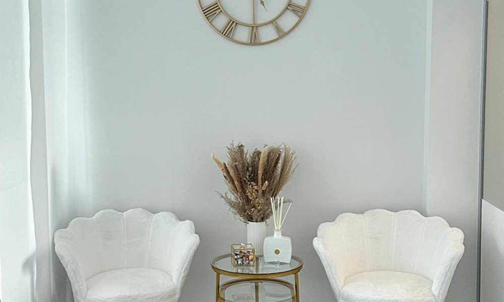 Foto von BEAUTY DREAMS Studio. Im Vordergrund die Behandlungsliege, der Stuhl, eine Lampe. Im Hintergrund Zertifikate in Rahmen an der Wand, ein SIdeboard und Dekoration